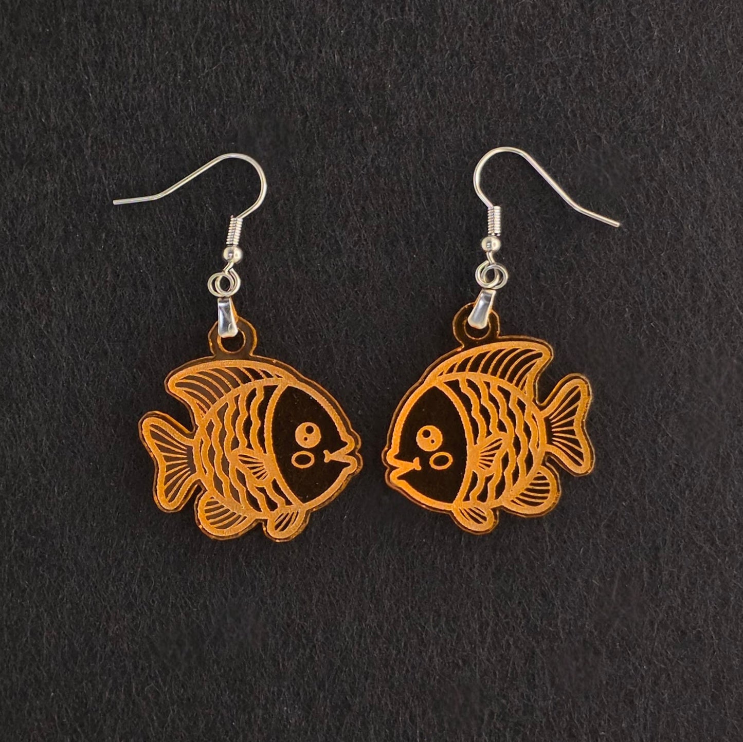 Handmade orange acrylic goldfish earrings with engraved detail, laser-cut and made to order, stainless steel hooks, shown on black background