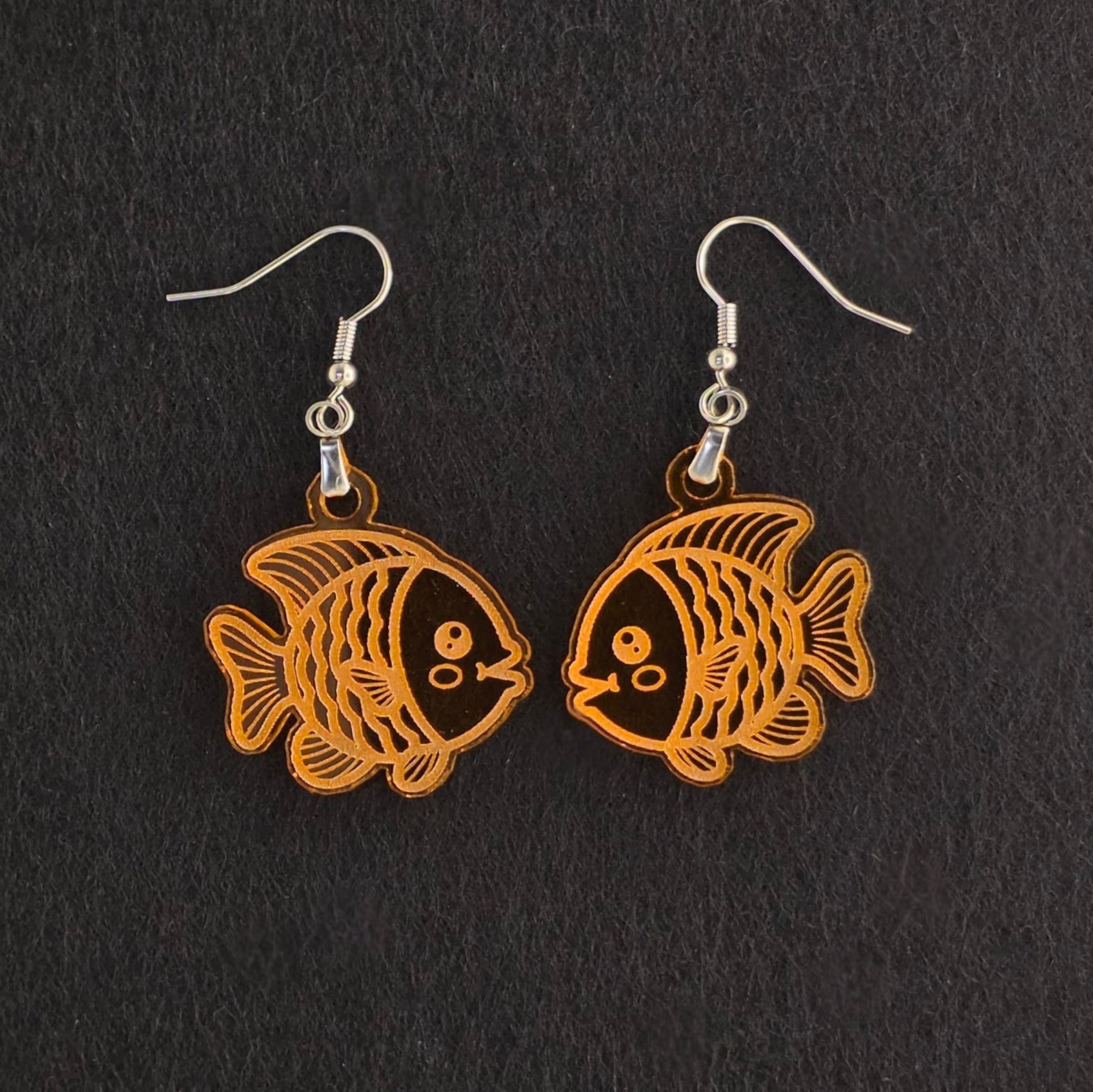 Handmade orange acrylic goldfish earrings with engraved detail, laser-cut and made to order, stainless steel hooks, shown on black background