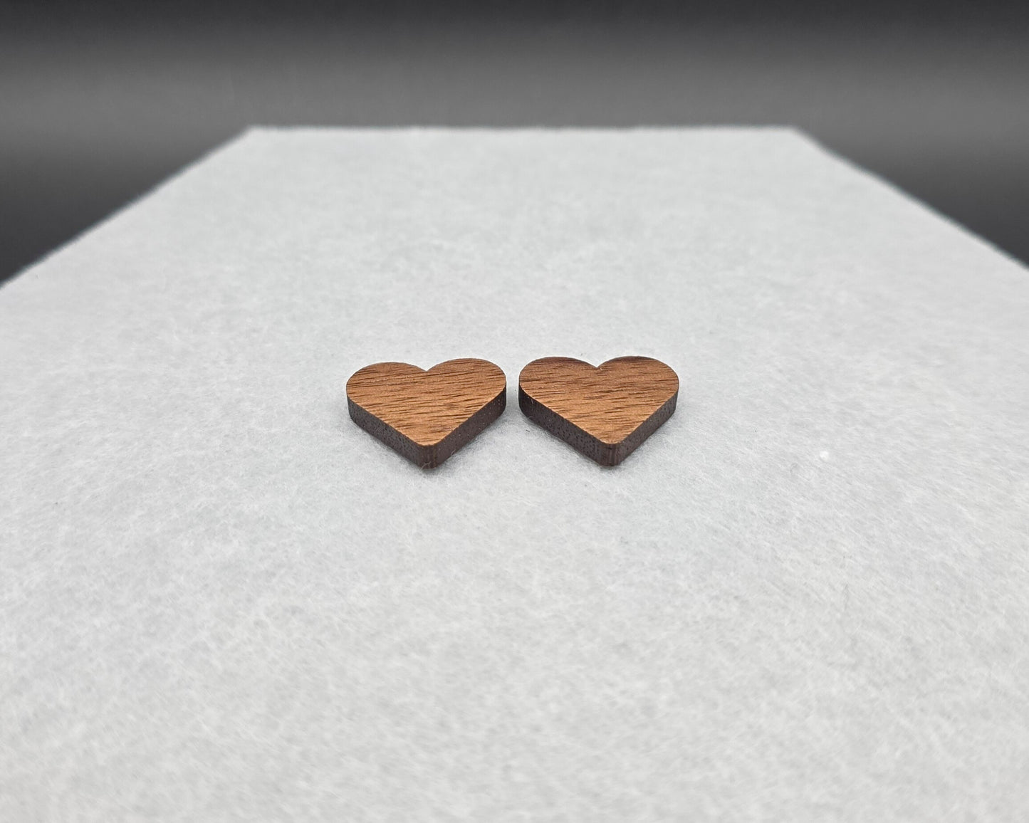 Walnut wood heart stud earrings at an angle showing thickness, handmade by Rainbow Charlie