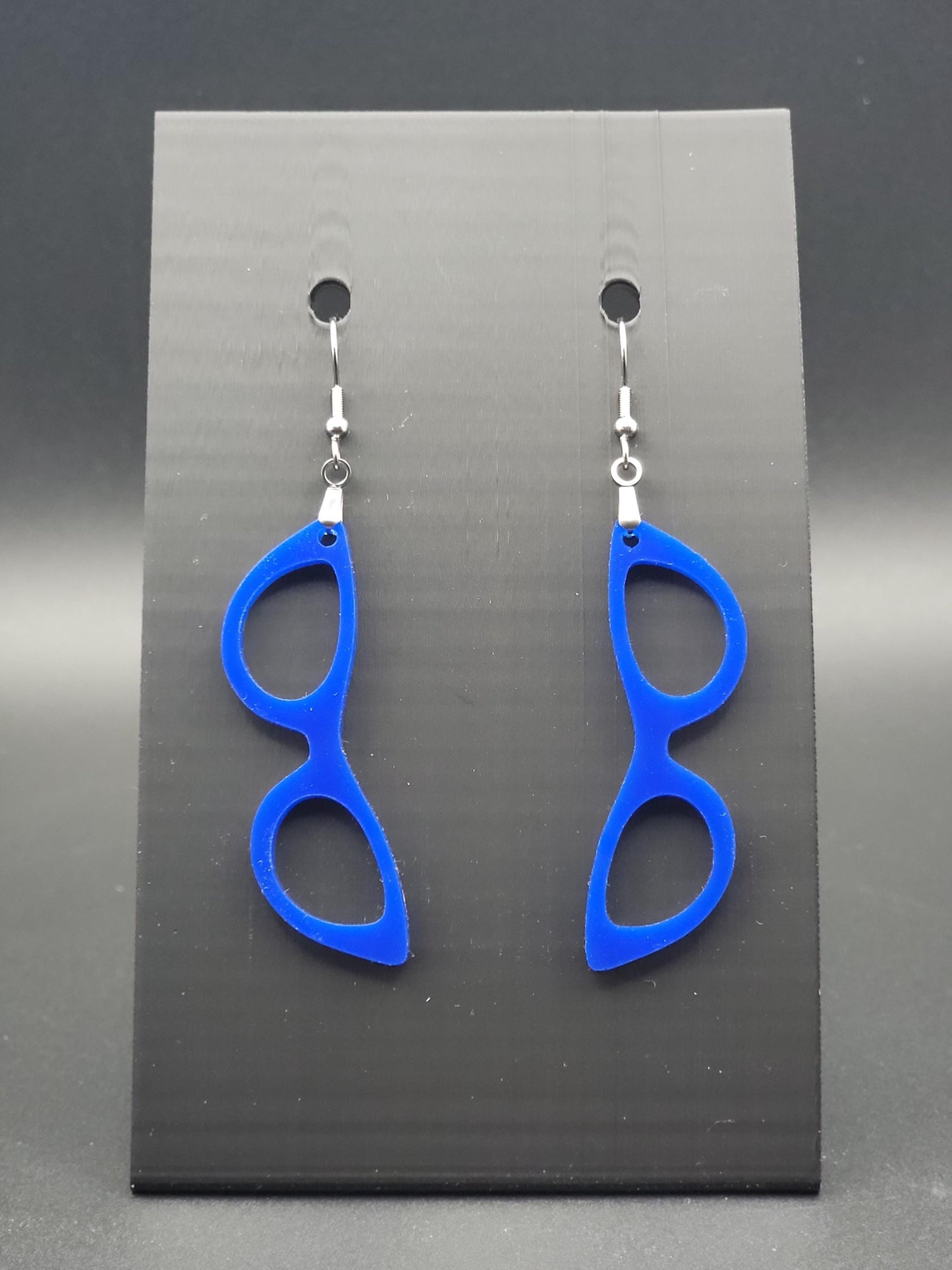 Blue acrylic cat-eye glasses dangle earrings on a matte black jewelry card. Handmade, laser-cut retro jewelry.