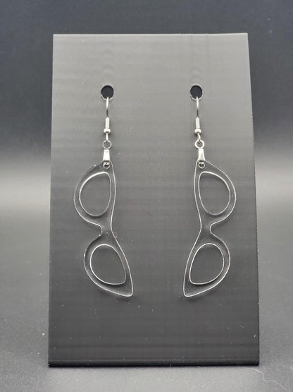 Clear acrylic cat-eye glasses dangle earrings on a matte black jewelry card. Handmade, laser-cut retro jewelry.