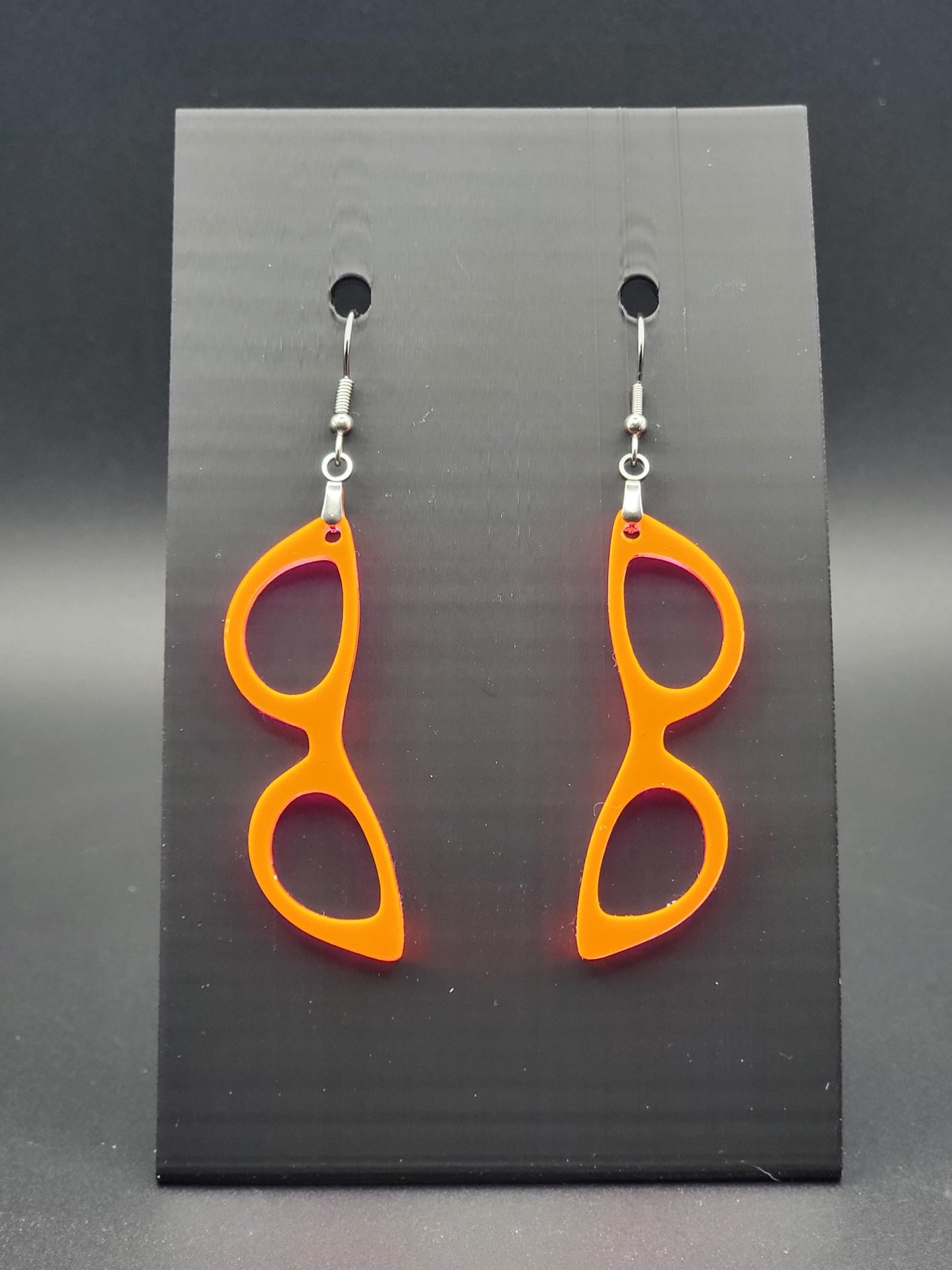 Fluorescent acrylic cat-eye glasses dangle earrings on a matte black jewelry card. Handmade, laser-cut retro jewelry.