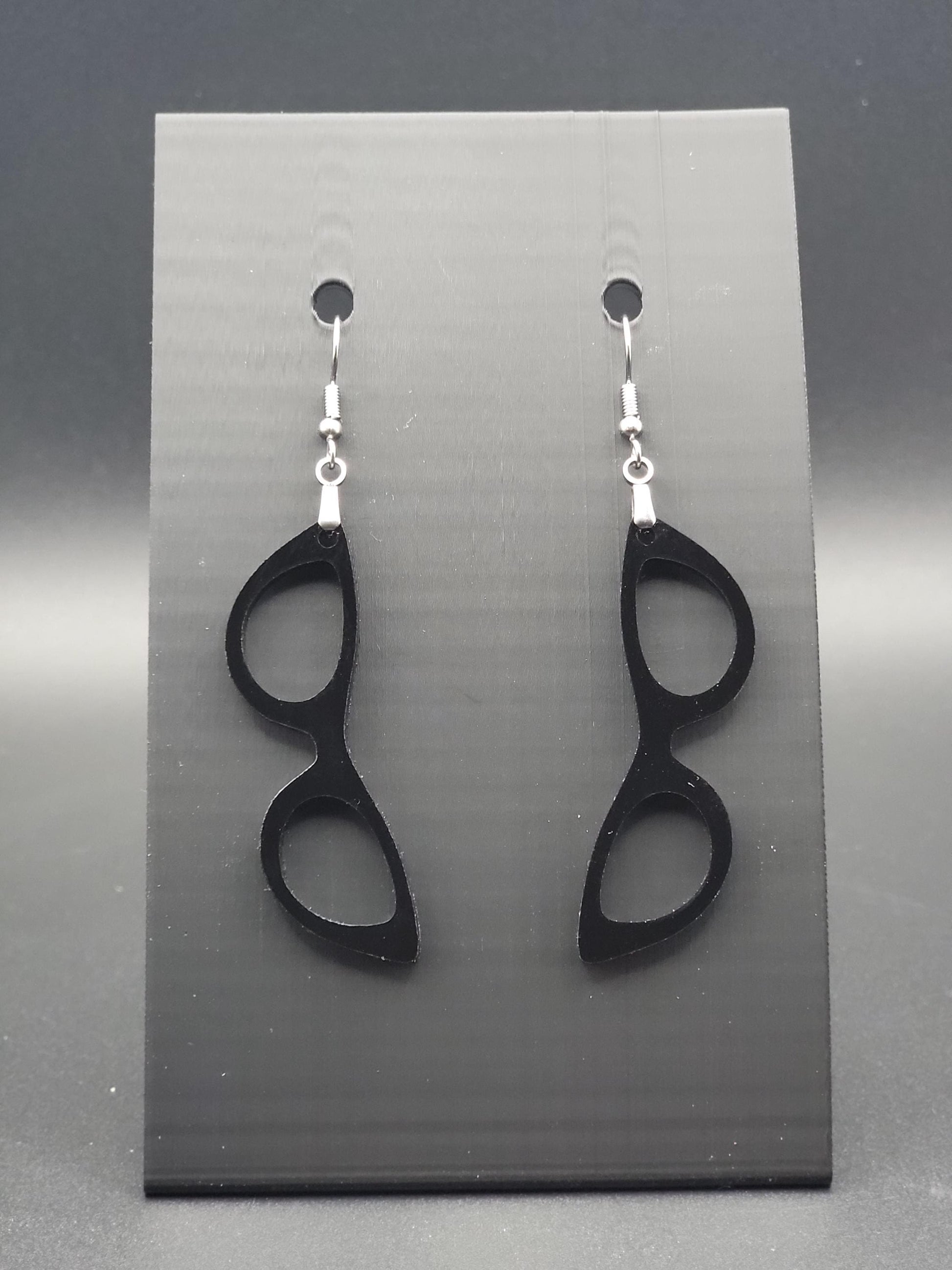 Black acrylic cat-eye glasses dangle earrings on a matte black jewelry card. Handmade, laser-cut retro jewelry.