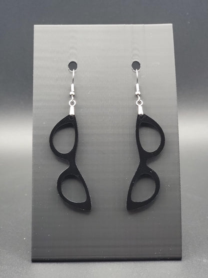 Black acrylic cat-eye glasses dangle earrings on a matte black jewelry card. Handmade, laser-cut retro jewelry.