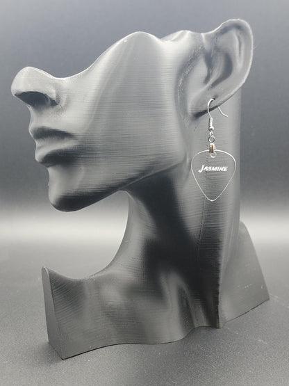 Clear acrylic guitar pick earring with "Jasmine" engraved, shown on a modern matte black mannequin head. Fun, personalized jewelry for music lovers.