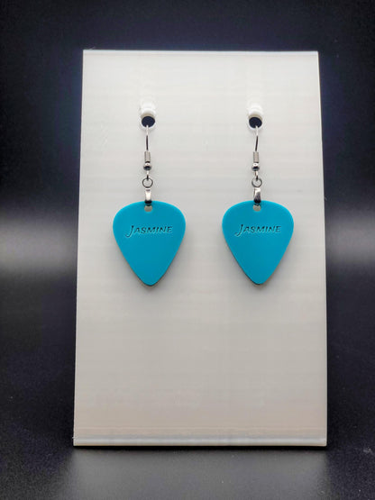 Teal acrylic guitar pick earring with "Jasmine" engraved, shown on a white jewelry card. Fun, personalized jewelry for music lovers.
