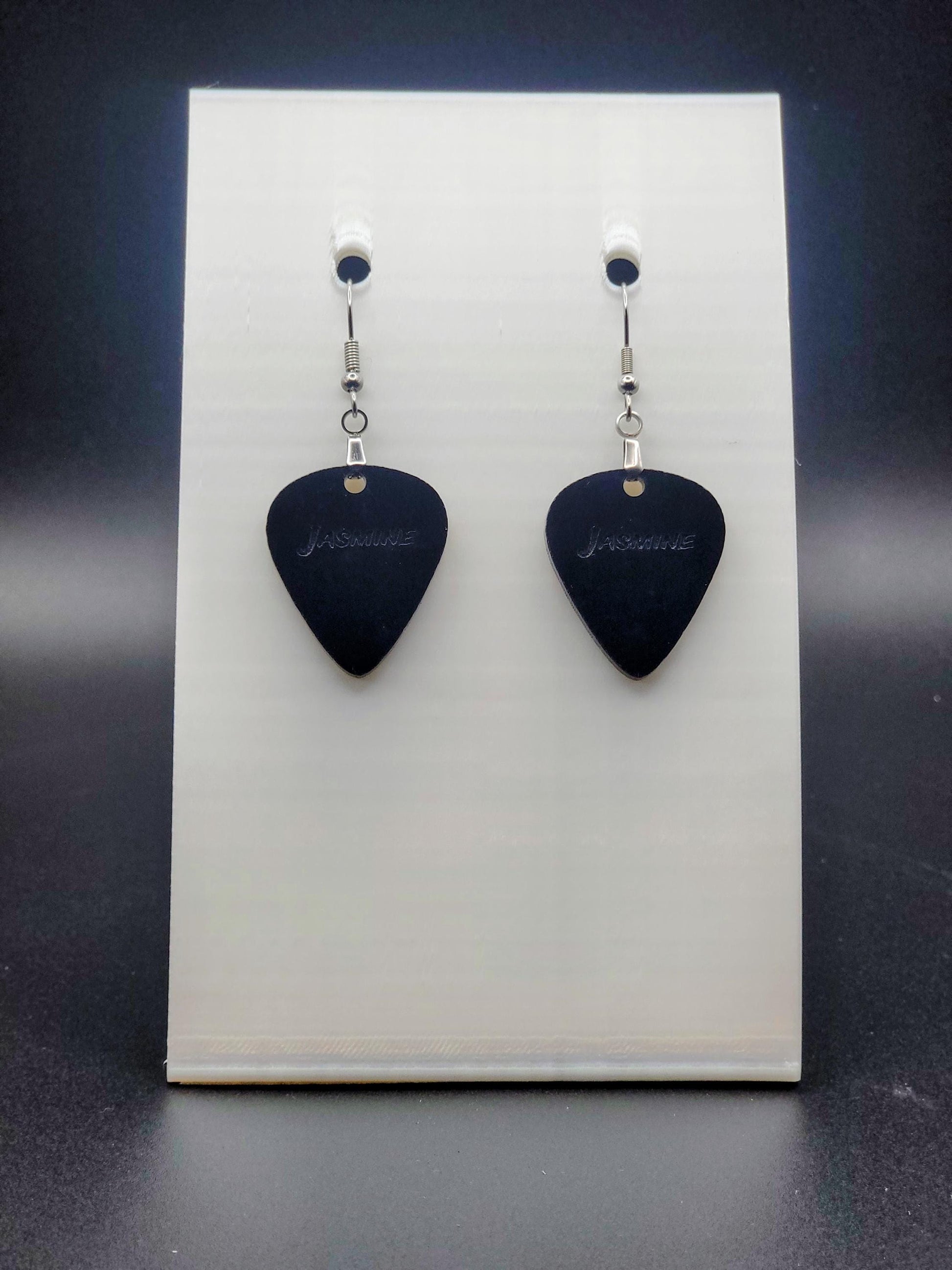 Black acrylic guitar pick earring with "Jasmine" engraved, shown on a white jewelry card. Fun, personalized jewelry for music lovers.