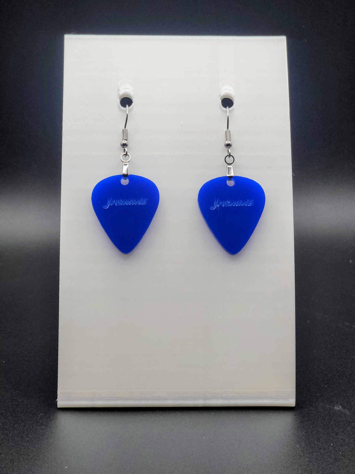 Blue acrylic guitar pick earring with "Jasmine" engraved, shown on a white jewelry card. Fun, personalized jewelry for music lovers.