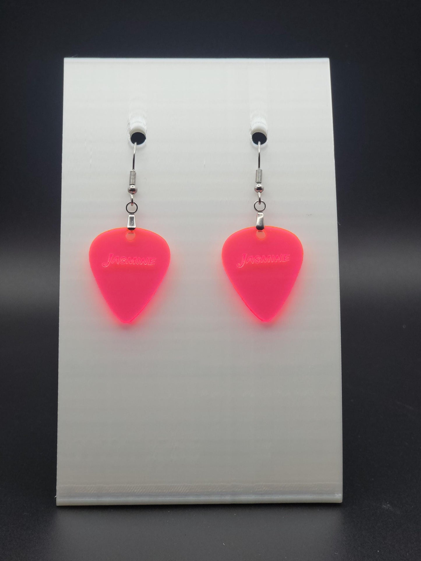 Fluorescent acrylic guitar pick earring with "Jasmine" engraved, shown on a white jewelry card. Fun, personalized jewelry for music lovers.