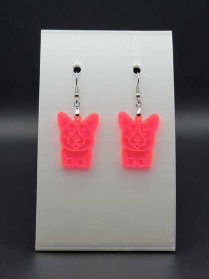 Pair of fluorescent acrylic corgi earrings engraved with a playful face. Shown on a white earring card.