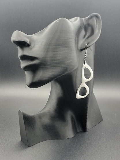 Single white dangle earring in the shape of cat-eye glasses on a black bust display, showcasing its bold, retro silhouette.