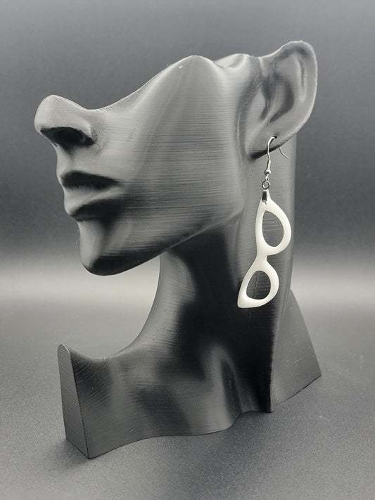 Single white dangle earring in the shape of cat-eye glasses on a black bust display, showcasing its bold, retro silhouette.
