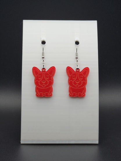 Pair of red acrylic corgi earrings engraved with a playful face. Shown on a black earring card.