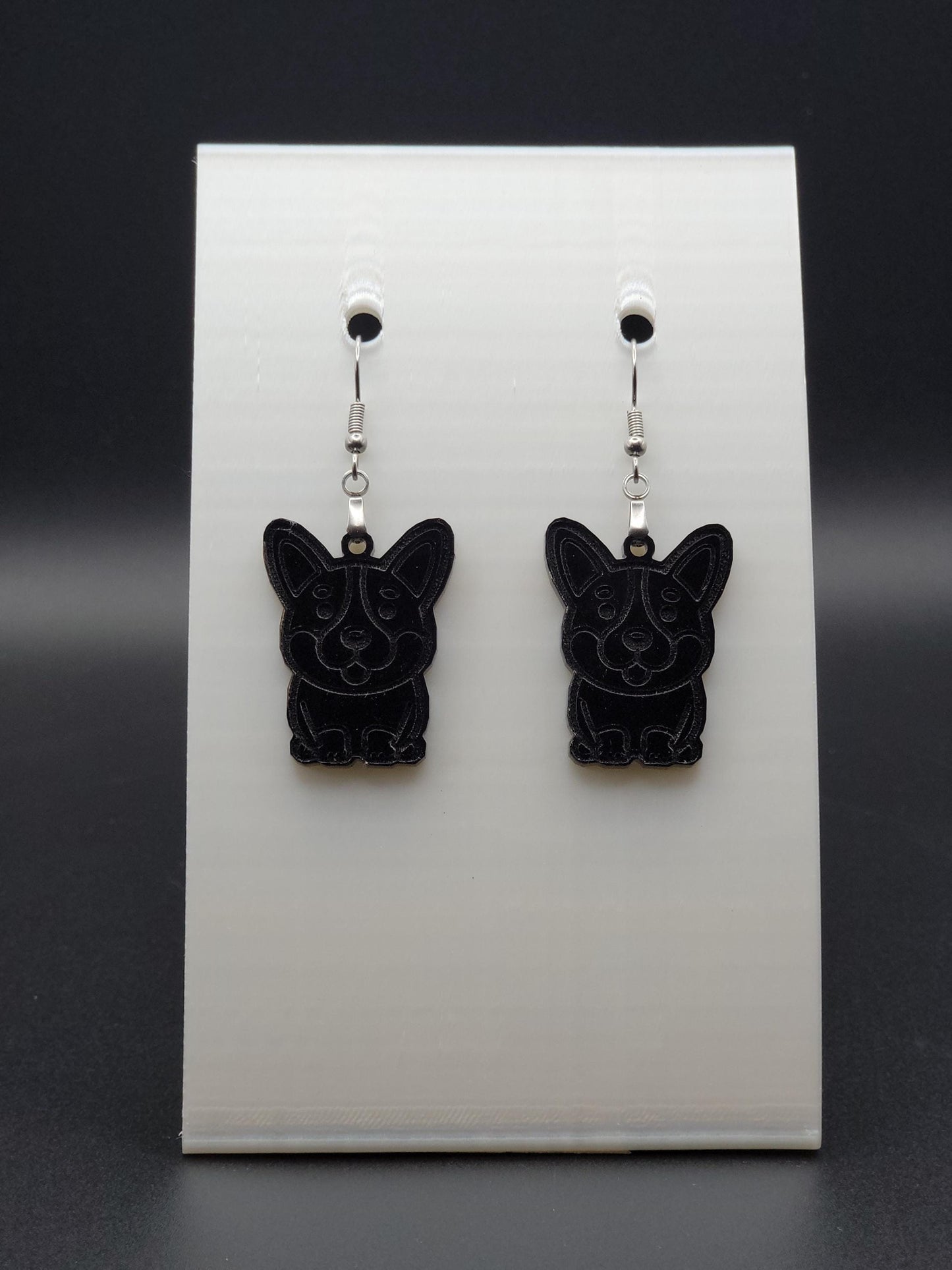 Pair of black acrylic corgi earrings engraved with a playful face. Shown on a white earring card.