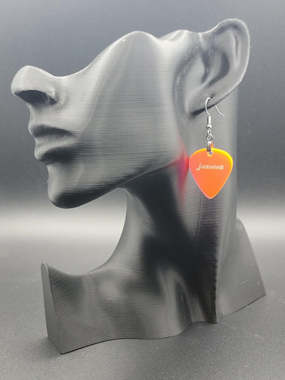 Fluorescent acrylic guitar pick earring with "Jasmine" engraved, shown on a modern matte black mannequin head. Fun, personalized jewelry for music lovers.