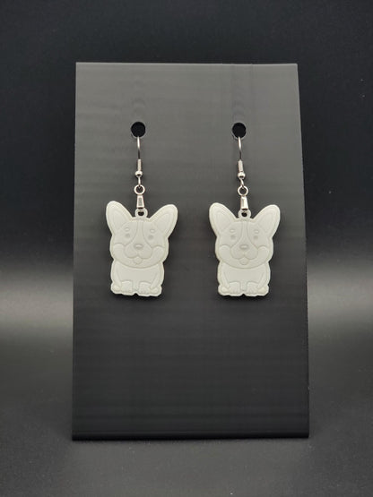 Pair of white acrylic corgi earrings engraved with a playful face. Shown on a black earring card.