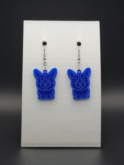 Pair of blue acrylic corgi earrings engraved with a playful face. Shown on a black earring card.