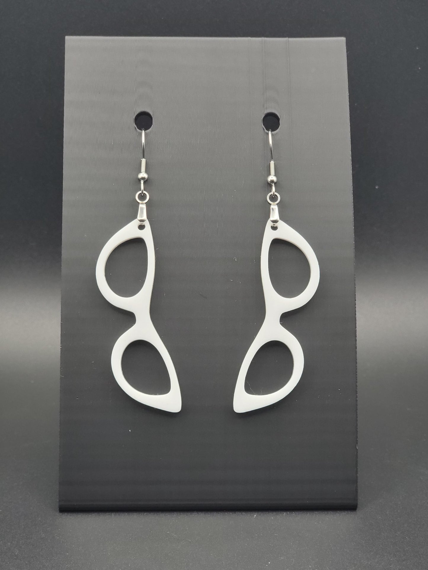 White acrylic cat-eye glasses dangle earrings on a matte black jewelry card. Handmade, laser-cut retro jewelry.