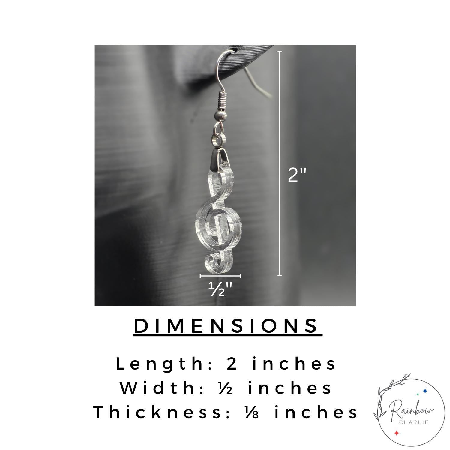 Close-up of clear acrylic treble clef earring with dimension overlay text. Measurements shown: 2 inches long, ½ inch wide, ⅛ inch thick.