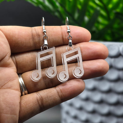 Pair of clear acrylic music note earrings with stainless steel hooks displayed on an open palm in front of a blurred plant background. Shows size and transparency of the earrings.