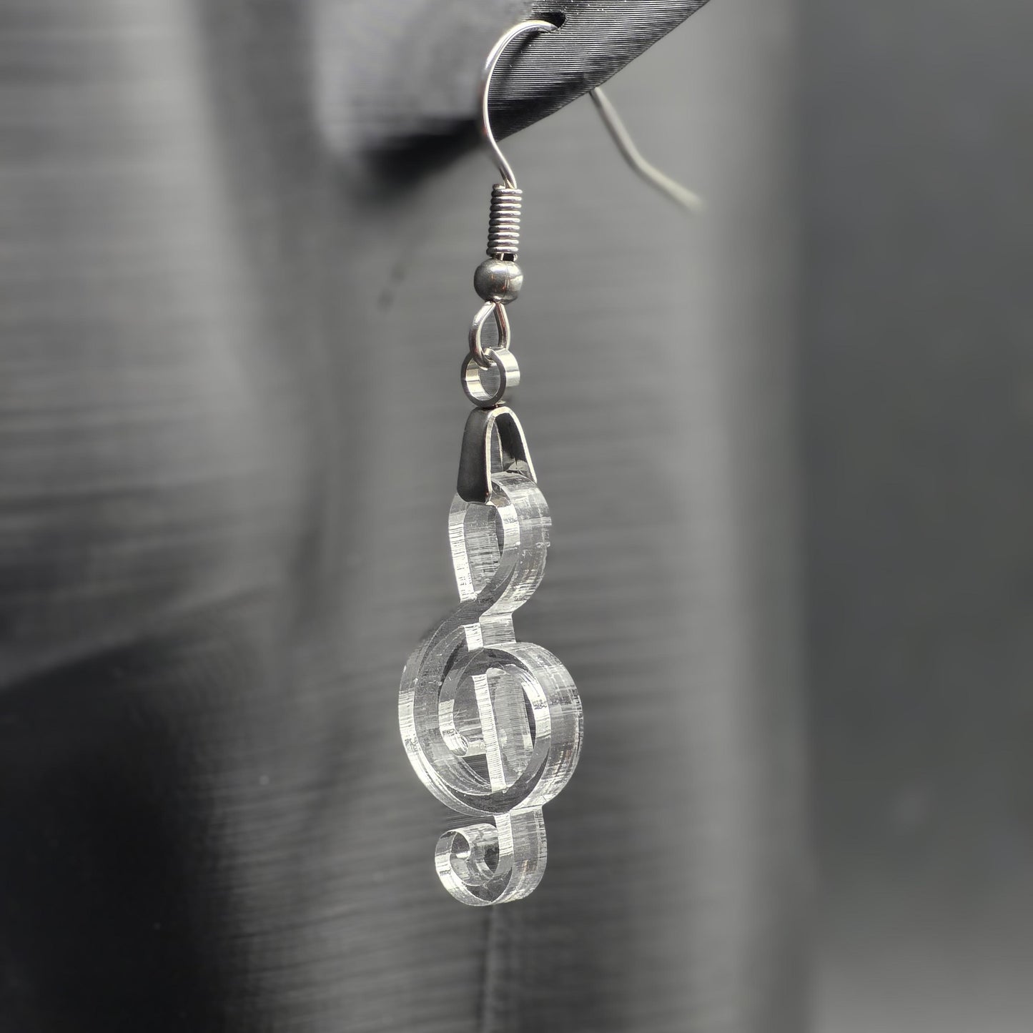 Clear acrylic treble clef earring on matte black mannequin ear, showcasing laser-cut detail and stainless steel hardware.