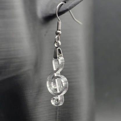 Clear acrylic treble clef earring on matte black mannequin ear, showcasing laser-cut detail and stainless steel hardware.