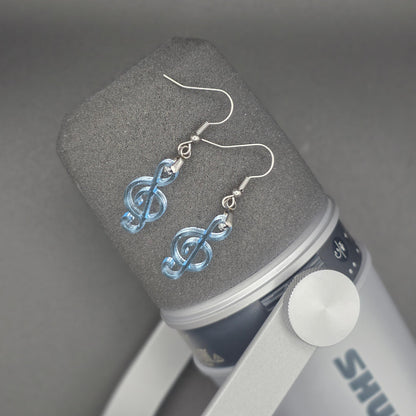 Clear blue acrylic treble clef earrings with stainless steel hooks hang from the head of a studio microphone.