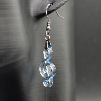 Clear blue acrylic treble clef earring on matte black mannequin ear, showcasing laser-cut detail and stainless steel hardware.