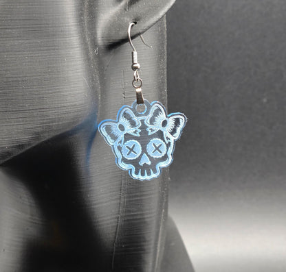 Clear blue acrylic skull earring with etched bows displayed on a black mannequin ear against a neutral gray background.