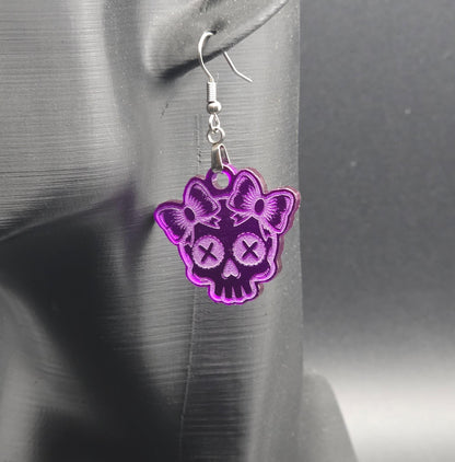 Single purple acrylic skull earring with bow details, hanging on a black mannequin ear with a dark gradient background.