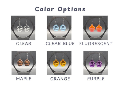 Grid showcasing six available color options for skull earrings: Clear, Clear Blue, Fluorescent, Maple, Orange, and Purple. Each pair is photographed on a black display stand, with legible white labels beneath each to highlight the vibrant and translucent finishes.