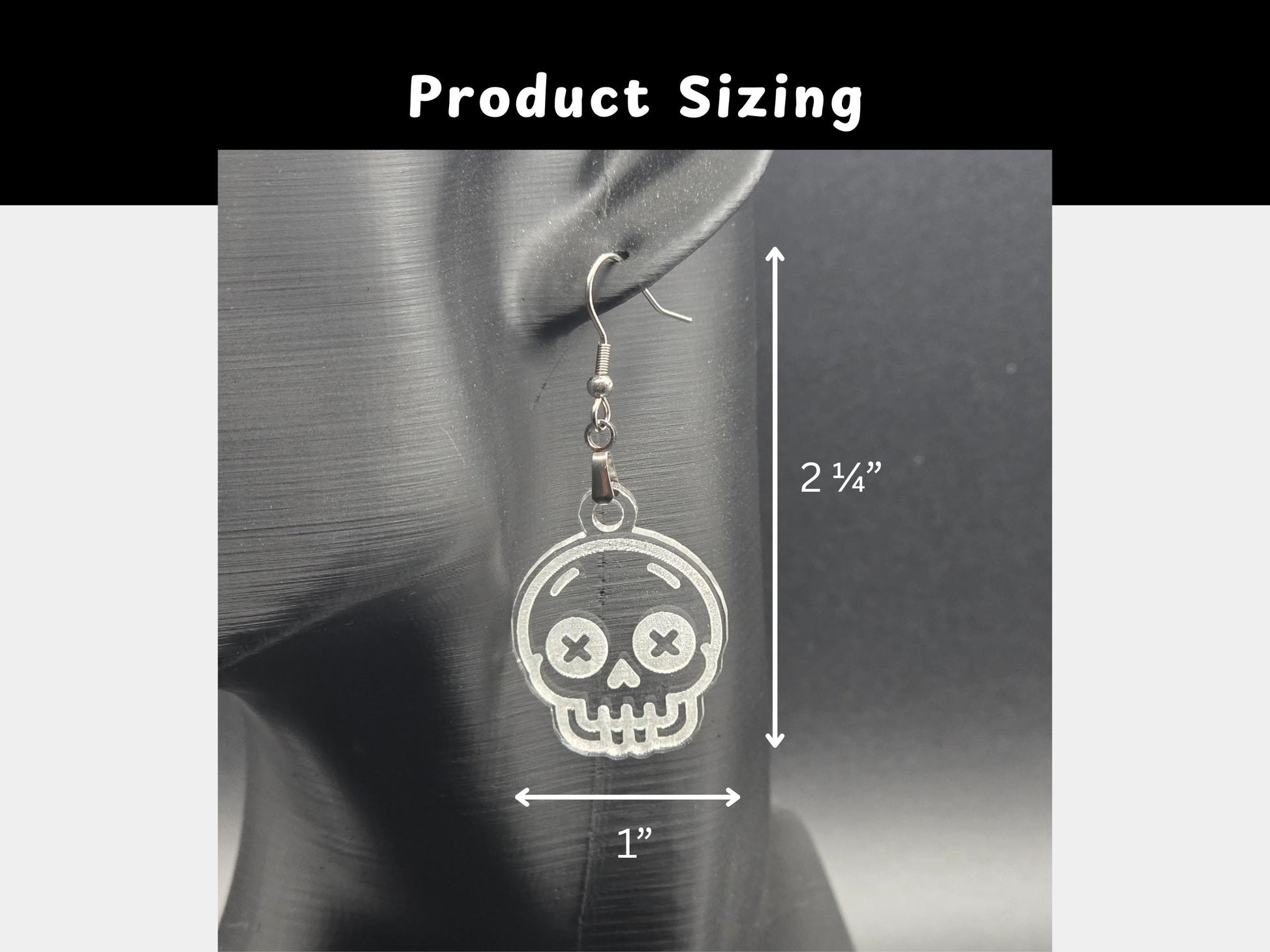 Clear acrylic skull earring displayed on a matte black mannequin head with measurements shown. Earring measures approximately 2¼ inches in length and 1 inch in width. White arrows and text provide visual scale for shoppers.