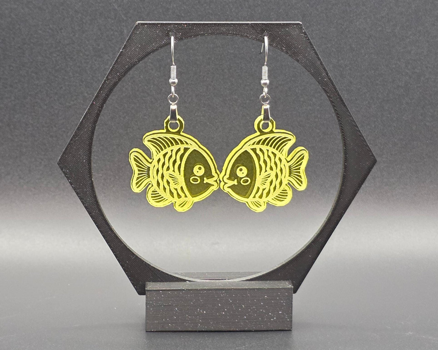 A pair of yellow acrylic goldfish earrings hanging from nickel-free hooks on a black display. The translucent yellow finish gives these handmade earrings a playful, sunny feel ideal for whimsical or nature-inspired styles.