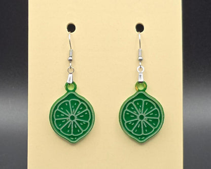 A pair of green acrylic lime slice earrings with stainless steel hooks hanging on a beige display card. The earrings are translucent and etched with citrus segment details for a fresh, juicy look.