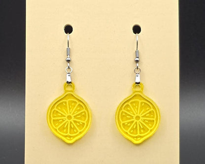 A pair of yellow acrylic lemon slice earrings with stainless steel hooks displayed on a beige earring card. The citrus slices are bright, translucent, and laser-cut with detailed segment etching.
