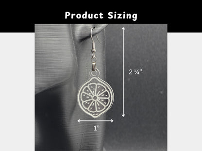 Close-up of a clear acrylic citrus slice earring on a mannequin head with labeled arrows showing measurements: 2¼ inches long and 1 inch wide. The background is dark for contrast.