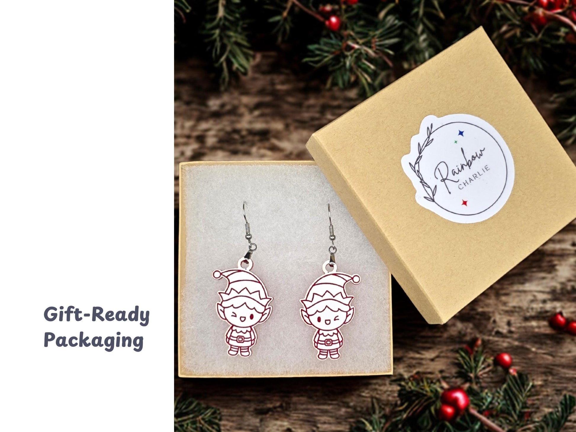 Elf earrings displayed inside a kraft jewelry gift box lined with soft white padding. The box lid, shown beside it, features a Rainbow Charlie logo sticker. Surrounding holiday greenery adds festive styling.