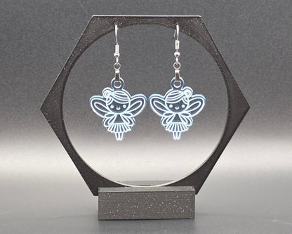 A pair of clear blue acrylic fairy earrings with engraved wing and dress details, hanging from nickel-free stainless steel hooks, displayed in a black hexagonal jewelry stand against a soft gray background. Handmade by Rainbow Charlie, whimsical and lightweight.
