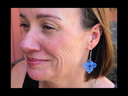 Close-up of a woman wearing clear blue acrylic fairy earrings from Rainbow Charlie. The handmade dangle earrings catch the light, showing their lightweight and whimsical design against a natural outdoor background.