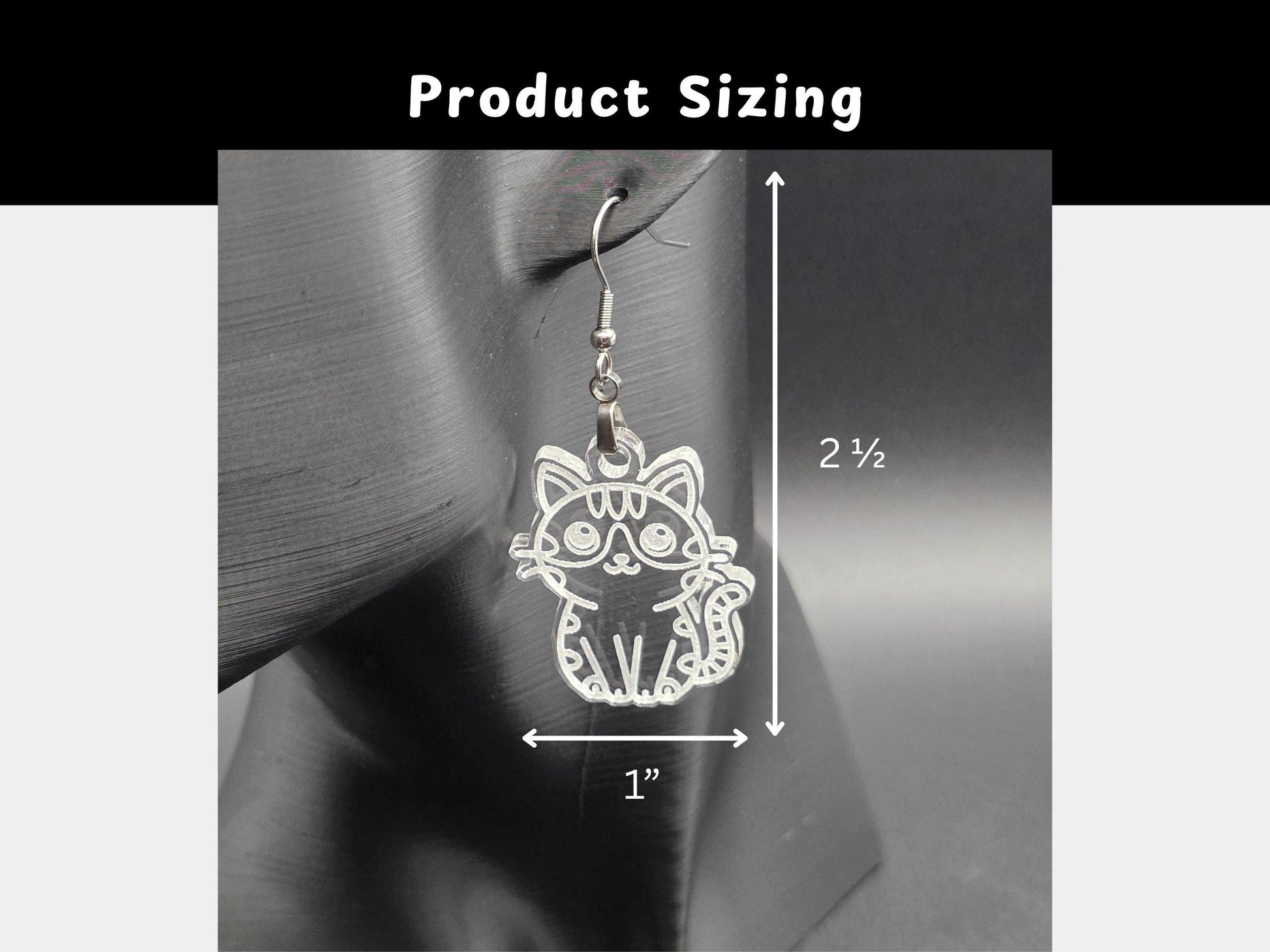 Close-up of a frosted acrylic cat earring hanging on a mannequin head. White measurement lines indicate the earring size: approximately 2.5 inches long and 1 inch wide.