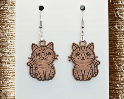 Walnut wood cat earrings with engraved line details, displayed on a white card. Textured brown scratching posts border the left and right sides of the image.