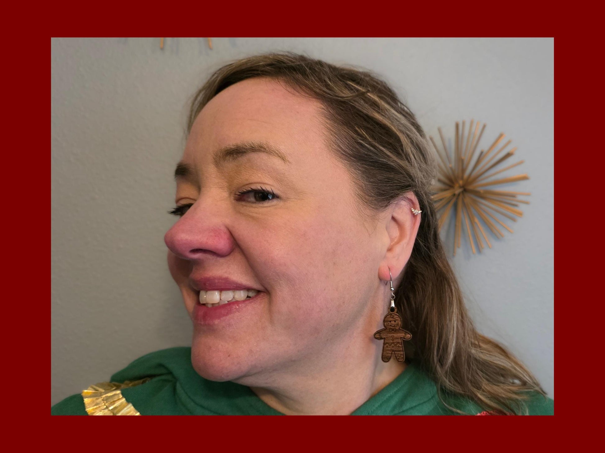 Woman smiling while wearing a single walnut wood gingerbread man earring. The lightweight handmade earring dangles from a nickel-free hook, highlighting comfortable, everyday wear.