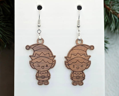 Front view of walnut wood elf earrings with laser-engraved dark details on natural grain, hanging from nickel-free stainless steel hooks on a white display card.