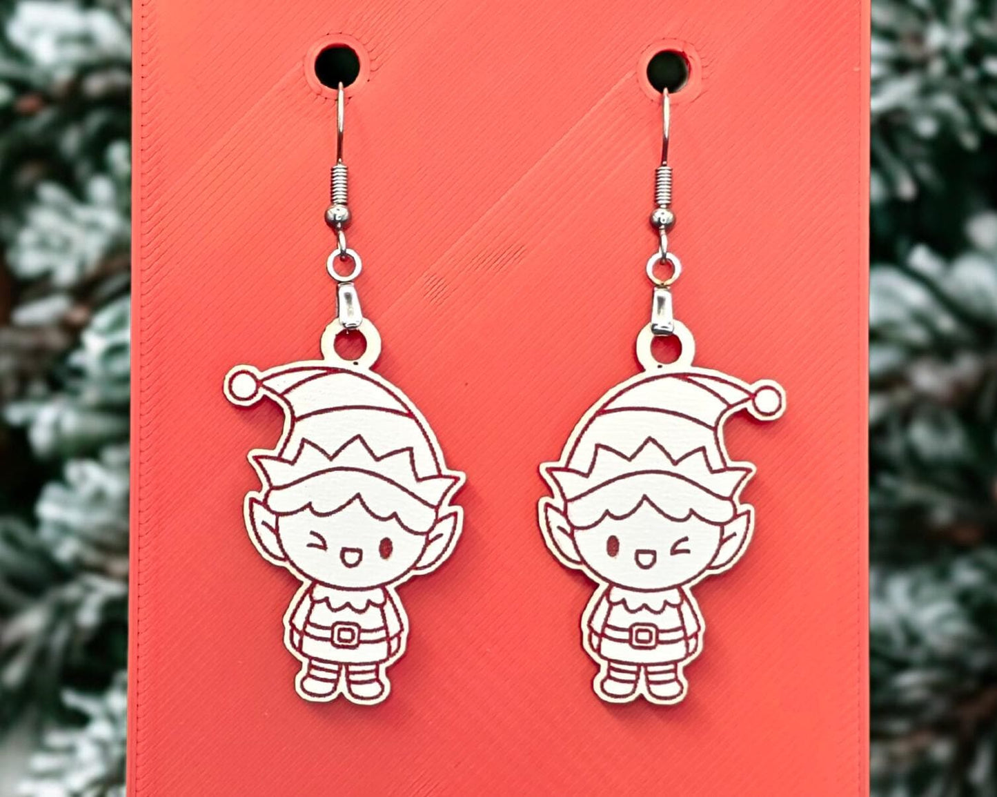Front view of white acrylic elf earrings with crisp red engraved details, hanging from stainless steel hooks on a red display card.