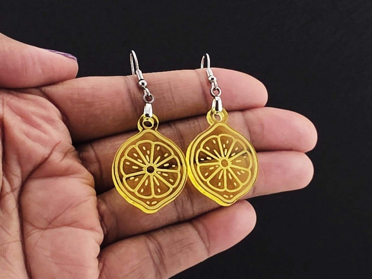 Lemon slice earrings resting in an open palm on a charcoal background, shown for scale.