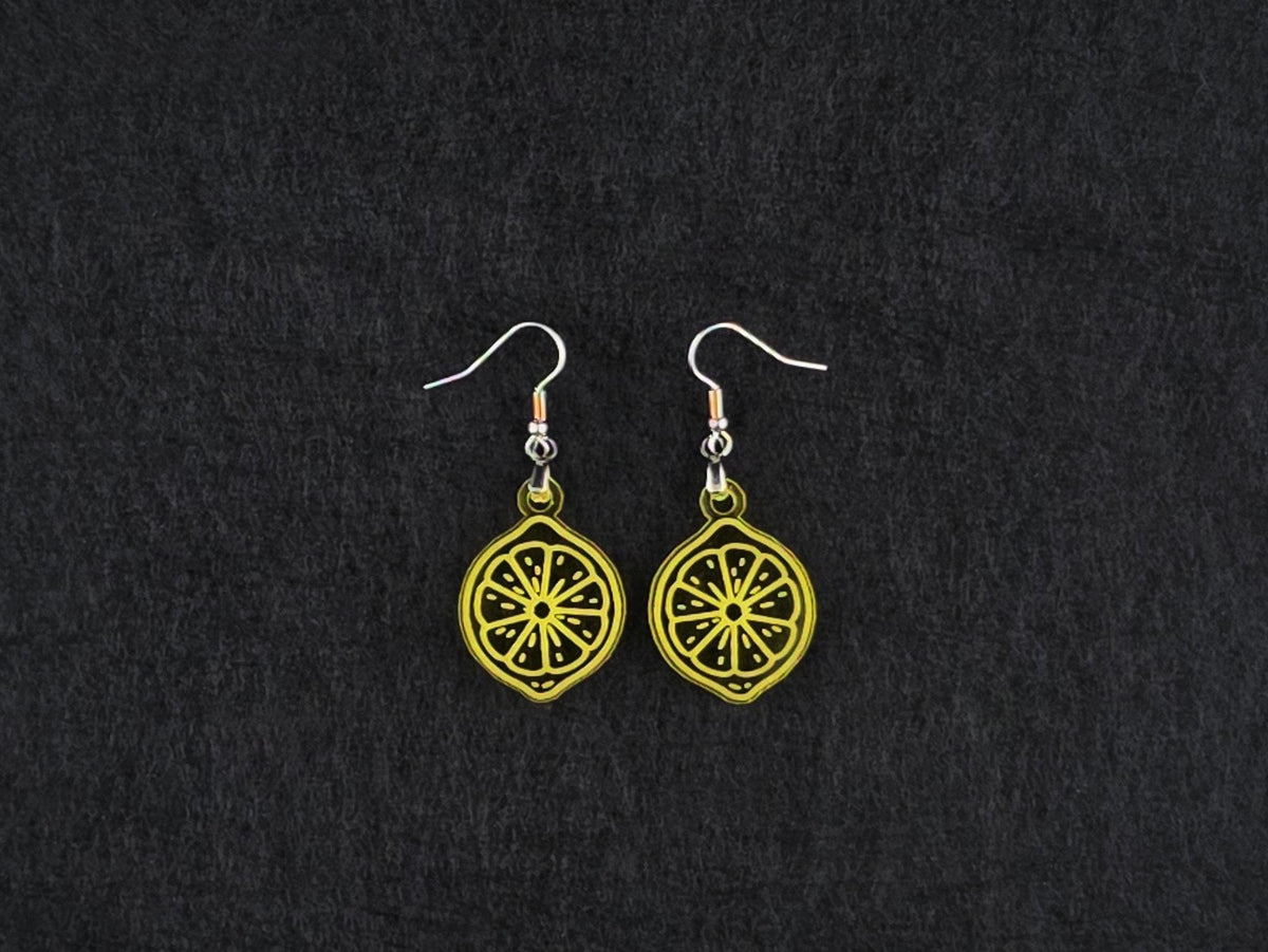 Pair of transparent yellow acrylic lemon slice earrings on stainless steel ear wires, flat lay on a charcoal background.