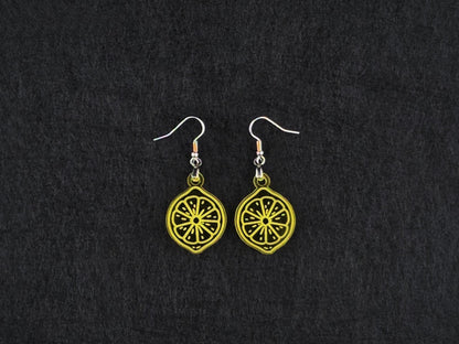 Pair of transparent yellow acrylic lemon slice earrings on stainless steel ear wires, flat lay on a charcoal background.