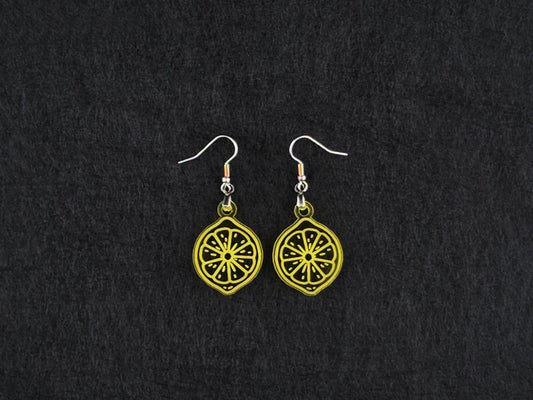 Pair of transparent yellow acrylic lemon slice earrings on stainless steel ear wires, flat lay on a charcoal background.