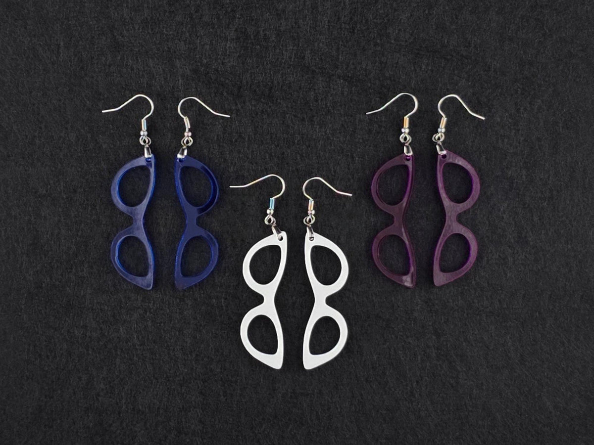 Three pairs of cat-eye earrings on charcoal in blue, white, and purple acrylic, showing three more colorways side by side.