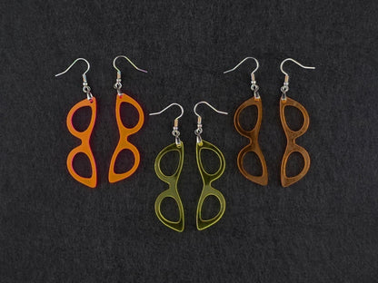 Three pairs of cat-eye earrings on charcoal in fluorescent orange-pink, translucent yellow, and amber orange acrylic, showing three colorways side by side.